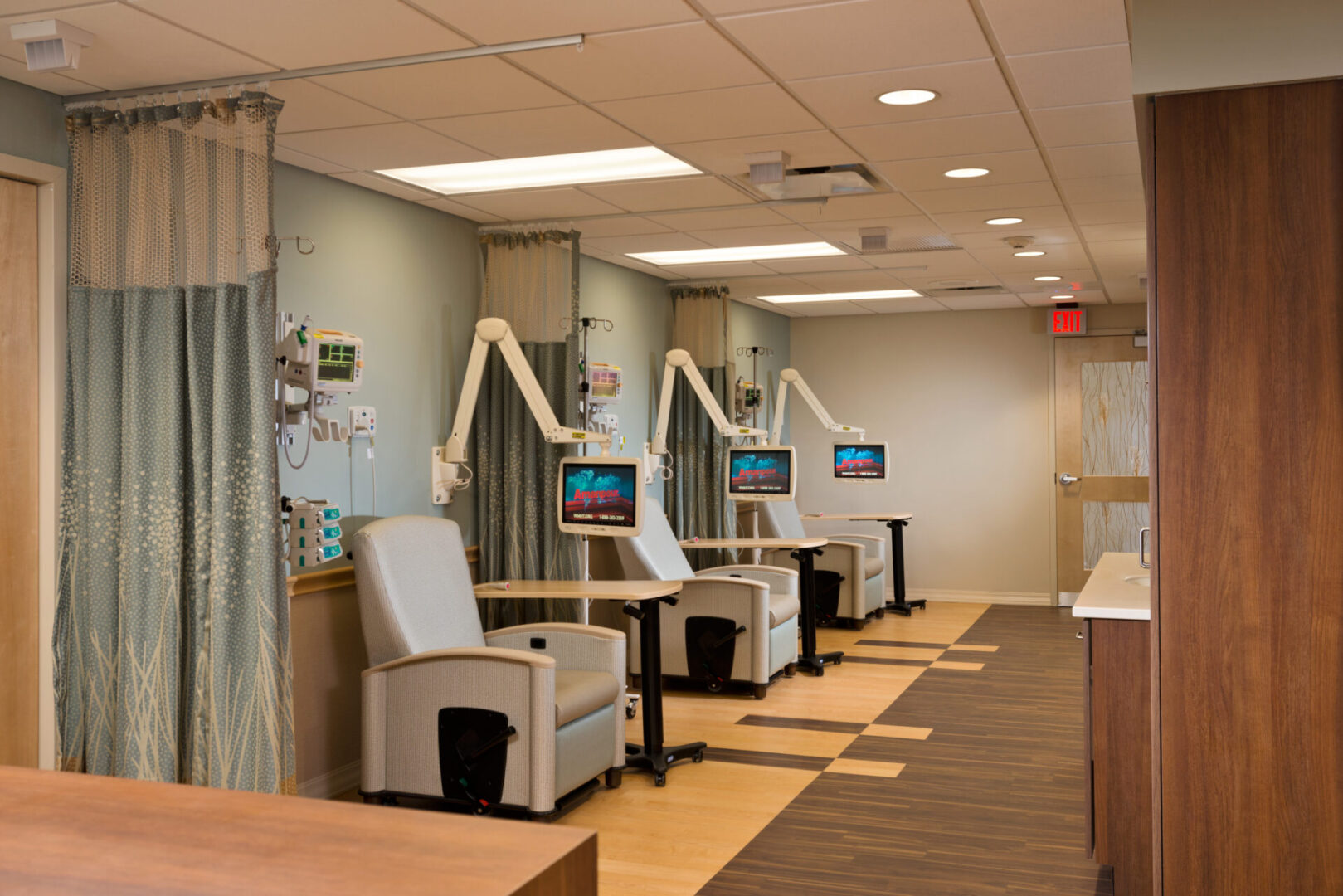 A hospital room with chairs and monitors on the wall.